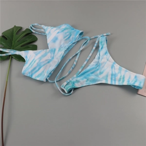 Vue à plat d'un bikini tie-dye bleu et blanc avec de fines bretelles et feuilles tropicales