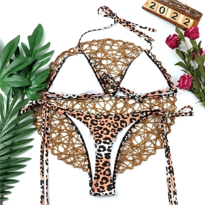 Flat lay of leopard print bikini set on straw mat with tropical leaves and roses