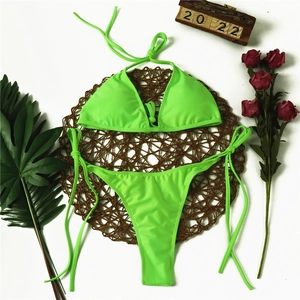 Flat lay of neon green triangle bikini set with halter top and side-tie bottoms on a mat