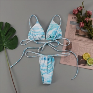 Flat lay of blue and white tie-dye triangle bikini with tropical leaves and magazine