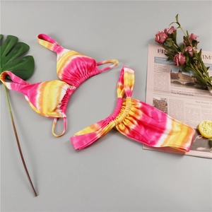 Detailed flat lay of pink and orange tie-dye bikini with ruched straps and tropical leaves