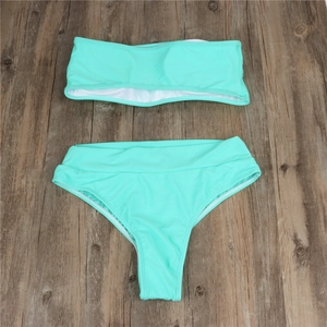 Flat lay of a mint green bandeau bikini set with high-waisted bottoms on wooden texture