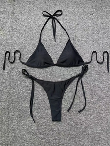 Flat lay of a black halter bikini set with side-tie bottoms on a grey textured background