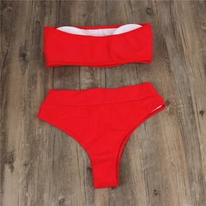 Flat lay of red strapless bandeau bikini top and high waisted bottoms on wood background