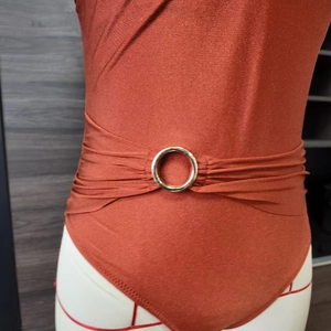 Detail of rust red swimsuit featuring a gold metal ring and elegant waist pleats