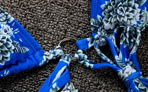 Detailed close-up of blue floral bikini with decorative metal O-ring and fine stitching