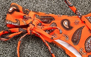 Gros plan du tissu de bikini orange à motif paisley avec lien de serrage latéral réglable