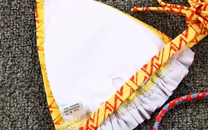 Detailed macro view of yellow bikini fabric showing inner lining and care label with S size