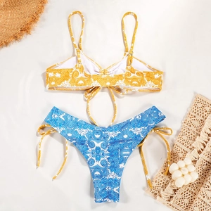 Flat lay of baroque print bikini set with blue and yellow patterns on sandy background