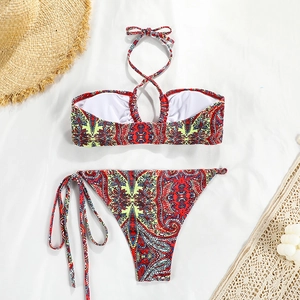 Flat lay detail of paisley print bikini set with straw hat and woven bag on white fabric