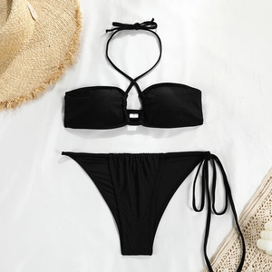 Flat lay of black halter bikini set with lace-up detail and straw beach accessories