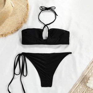 Flat lay of black bandeau bikini set with tie details and textured fabric on white decor