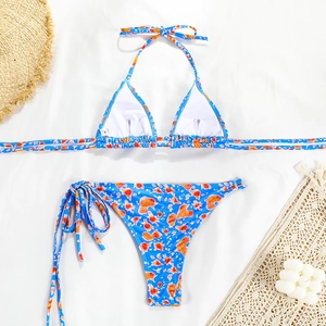 Flat lay of blue bikini with orange prints, neck strap detail, and summer accessories