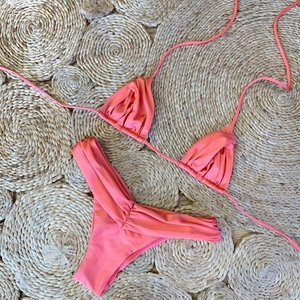 Detailed view of coral pink textured bikini set with ruched back bottoms on straw mat