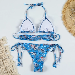 Flat lay of floral paisley lace bikini set with straw hat on minimalist background