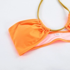 Détail du haut de bikini orange avec lanières dorées montrant l'étiquette et les coutures