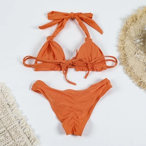 Flat lay of an orange bikini set with knot details, straw hat, and summer beach accessories