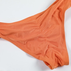 Detailed view of bright orange scrunch bikini bottom made of shiny metallic nylon fabric