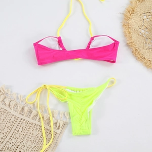 Détail d'un bikini bicolore rose vif et jaune fluo posé sur une natte de plage bohème