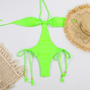 Flat lay of a neon green halter monokini with cut-outs, tassel ties and beach accessories