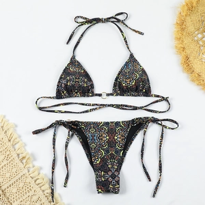 Flat lay of mandala print bikini set with golden ring accent on a white beach set