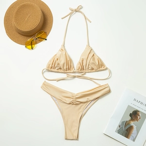 Flat lay of champagne gold bikini set with textured fabric on beach resort background