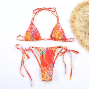 Flat lay of colorful marble print bikini set with metal rings and summer straw hat