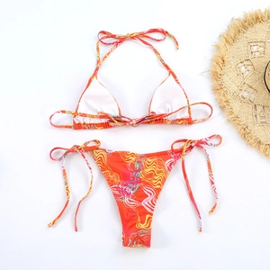 Flat lay of a vibrant orange wavy print bikini set with side-tie bottoms and a beach hat