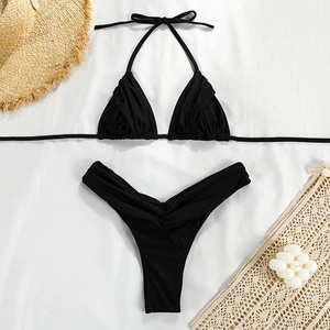Flat lay of black pleated two-piece bikini set with straw hat on a white background
