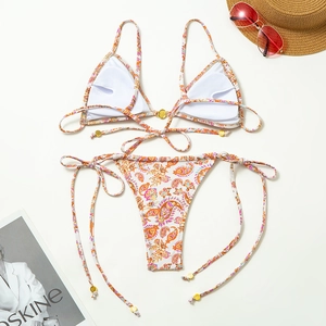 Detailed flat lay of colorful paisley print bikini with beach accessories and sun hat