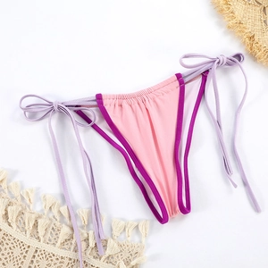 Flat lay of pink bikini bottoms with purple piping and side ties on a beach setup
