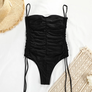 Détail d'un maillot de bain une pièce noir froncé avec de fines bretelles sur décor plage