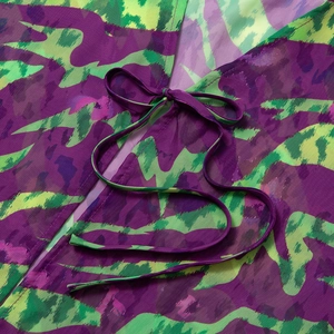 Detail of printed chiffon top featuring purple and green tie-dye pattern and bow neckline