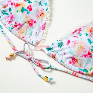 Dettaglio del top bikini floreale con pizzo, fiocco rosa e perla dorata con corona