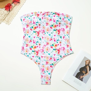 Flat lay of floral bandeau swimsuit with bow detail, sun hat, and sunglasses on white