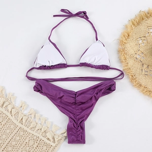 Detail view of purple ruched bikini bottom with neck tie top on summer beach props
