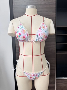 Dettaglio del bikini floreale con pizzo bianco e fiocco rosa su un manichino industriale