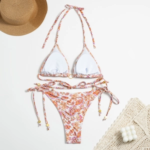 Flat lay of floral bikini with golden rings, sun hat, and beach accessories on white surface