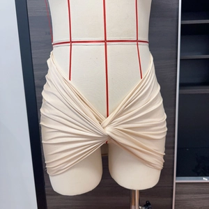 Dettaglio mini gonna beige a vita alta con nodo a intreccio e finiture a pieghe