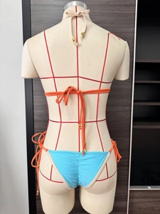 Detail of blue bikini bottom with orange side ties and gold metallic accents on the strings