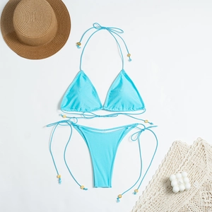Flat lay of light blue bikini set with gold bead details and summer holiday decorations