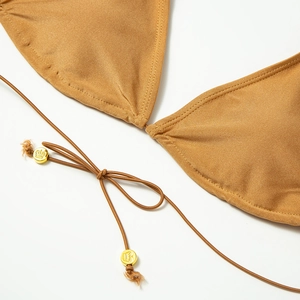 Detail of ochre bikini top featuring adjustable straps and gold crown embossed metal beads