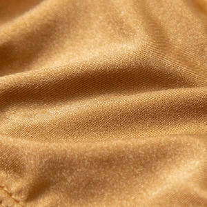 Macro shot of gold nylon bikini fabric with shimmering metallic texture and fine weave
