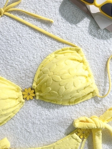 Bright yellow two-piece floral bikini with daisy charms on soft white plush background