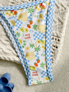 Tropical fruit print bikini bottoms with checkered trim on beige knit background