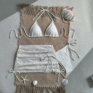 Dettaglio di un set bikini a tre pezzi in pizzo bianco con pareo coordinato