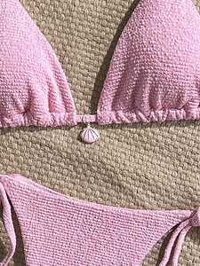Pink two-piece crinkle fabric bikini set featuring a seashell pendant on a woven mat