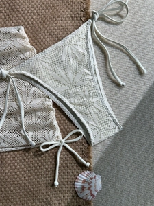 Dettaglio del bikini in crochet avorio con pizzi floreali e bordi decorati di perle