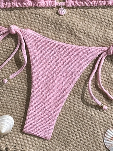 Pink seersucker bikini with adjustable side ties and metallic beads on a beach mat