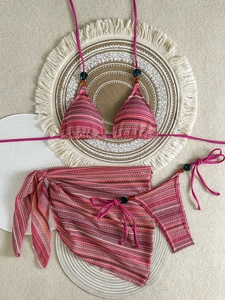 Flat lay of a 3-piece knit bikini set with halter top, side-tie bottoms and beach sarong